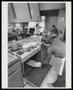 Photograph: [A mother cooking while a father sits with two kids]