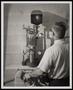 Photograph: [A man turning a machine's circular handles]