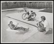 Photograph: [A man and a woman next to a pool a second man floats in]