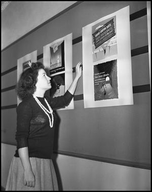 Primary view of object titled '[Young woman looks at a poster on the wall]'.