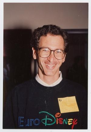 Man with glasses and dark blue Euro Disney sweater, with a white collared shirt.