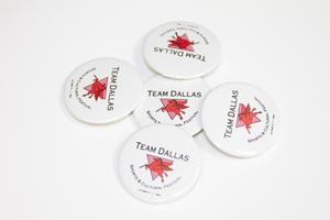 5 white buttons with the words Team Dallas on it. Under it is an upside down pink triangle with a red winged horse on it.