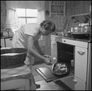 Primary view of object titled '[A woman pulling food from an oven]'.