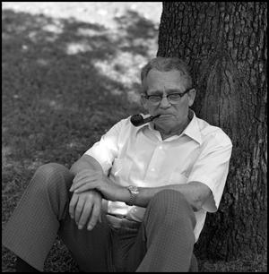 Primary view of object titled '[Dr. Wayne Adams  sits beneath a tree]'.