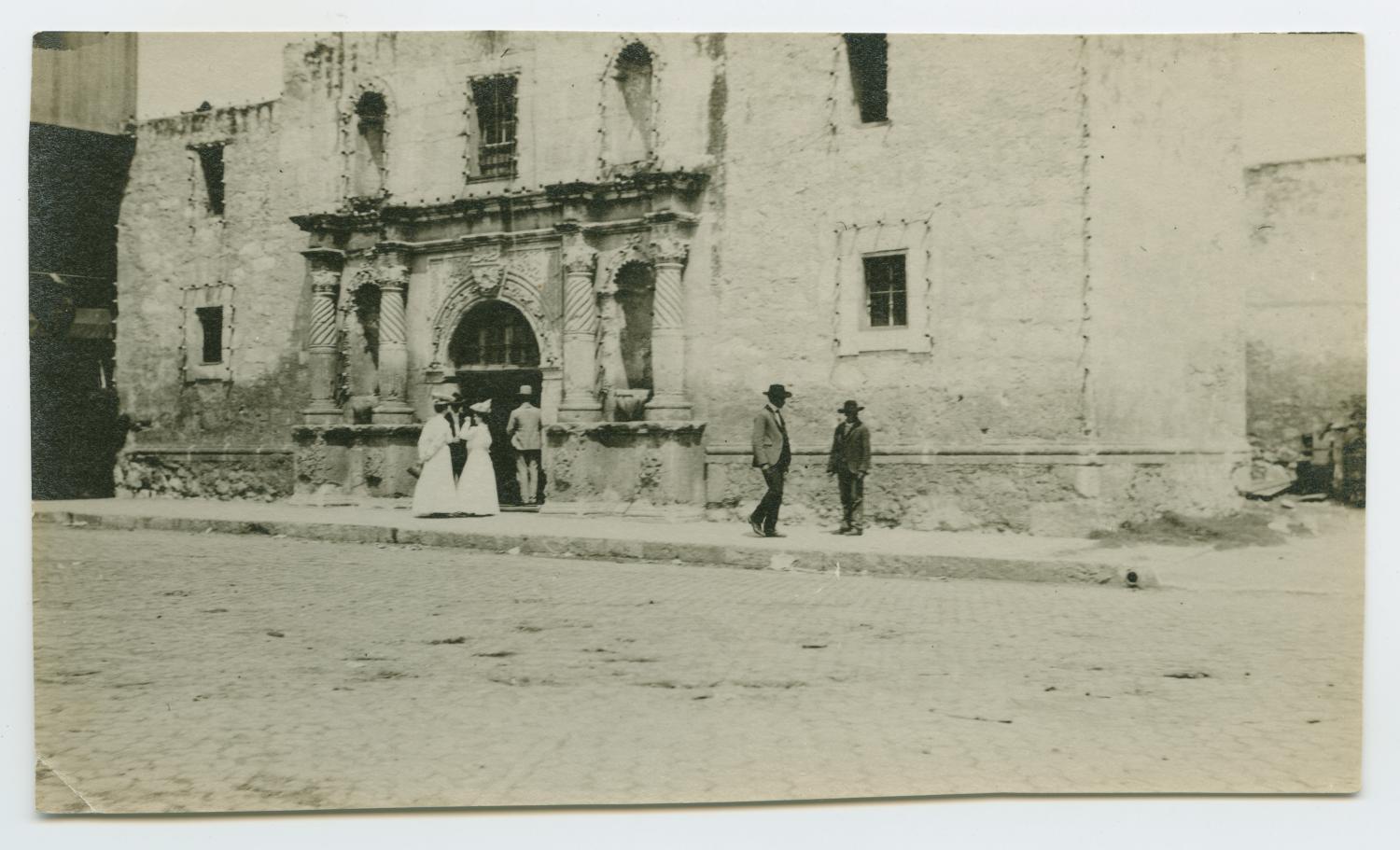 [People Visiting the Alamo], Photograph of a group of people in front of the Alamo between 1900-1930. There appear to be three men and two women outside of the building., 