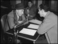 Photograph: [Two men sitting at a table with a microphone]
