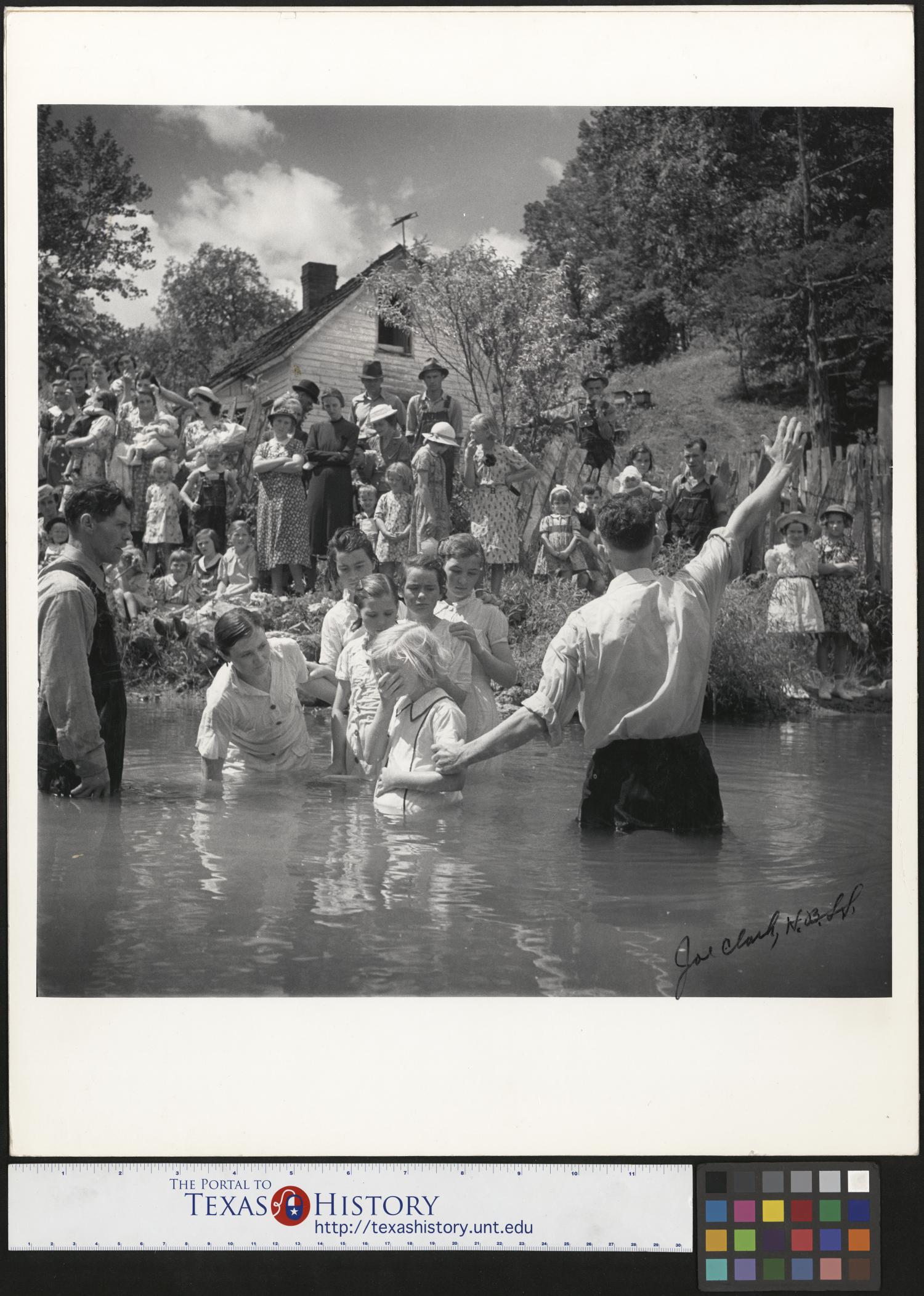 [Baptising in Olde Towne Creek], Photograph of the baptism of Ivana Wright, who is standing a creek next to Preacher Hugh Vancel; Vancel is facing the bank and raising one of his hands toward the crowd standing on the bank. Immediately behind them, Hester Welch, Minnie Hicks, Cleo McCurey, Lilian Hicks, and Lenore Treece are also in the creek, standing in line. The baptisms took place int he Olde Towne Creek outside John Owens home in Red Hill, Tennessee., 