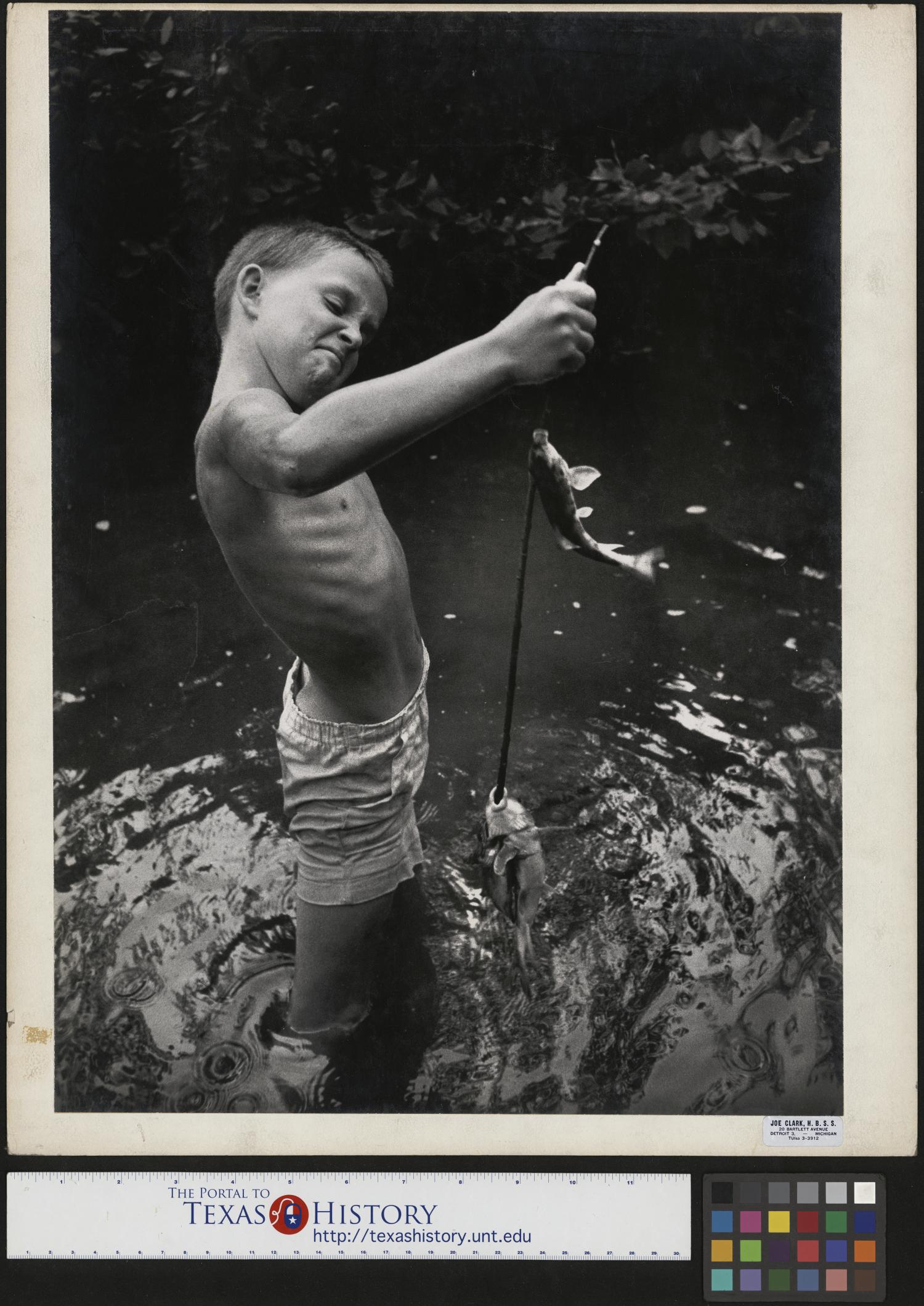 [Jimmy Powell Fishing], Photograph of an unidentified boy fishing, possibly in Lynchburg or Cumberland Gap, Tennessee. He wears shorts but no shirt and holds up his fish and pole., 