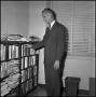 Photograph: [Dr. Edward Bonk grabbing a book from the bookcase]