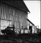 Photograph: [Photograph of a farm carriage sitting next to a barn]