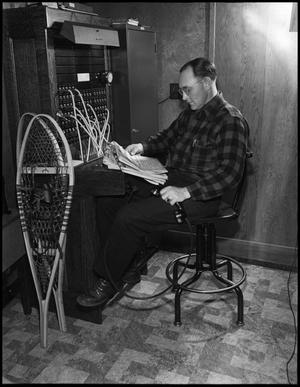 Primary view of object titled '[Man reading the newspaper at the telephone switchboard]'.