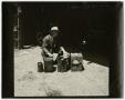 Photograph: [Man kneeling by square objects]
