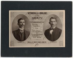 Un anuncio sobre una página de color negro. El anuncio tiene las imágenes de dos hombres con traje y corbatín, ambos con bigote. La parte superior del anuncio dice Kendall-Bruce y la parte inferior dice Nulla Dies Sine Linea.