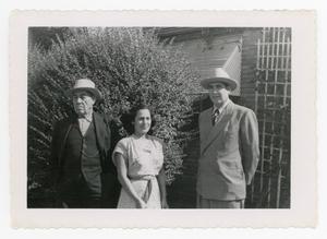Primary view of object titled '[Macario Cuellar, Mary Cuellar, and Frank Cuellar Sr. standing in front of a house]'.