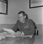 Photograph: [John Spencer Church in uniform sitting at a desk reading]