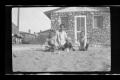 Photograph: [Irene Williams sitting in front of her house with her children]