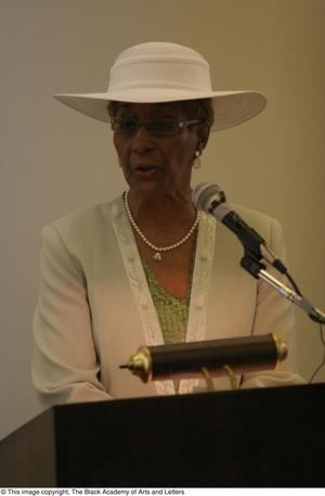 Primary view of object titled '[Woman in white hat standing at podium]'.