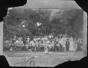 [Men, Women, and Children in front of a grove of trees]