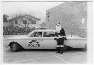 [Andy Anderson in City of Denton Police Car with Presents; Santa Claus Leans Against Car]