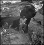 Photograph: [Man Kneeling in Cave Entrance]