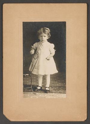 [Photograph of a Young Girl Standing Next to a Chair]