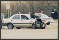 Photograph: [Damaged Sedan Stopped in Intersection]