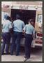 Photograph: [Three Paramedics Stand Behind Ambulance]
