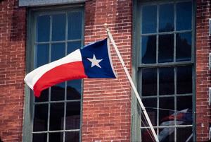[Photograph of Texas Flag in Front of Brick Building]