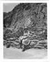 Photograph: [Helen Moore sitting at the base of a cliff in Frijoles Canyon, New M…