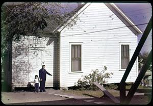 [Photograph of Man and Child in Front of White Building]