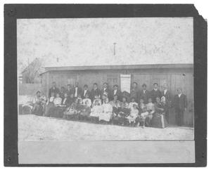 [Group Portrait in Front of a Small Wood-Slatted Building]