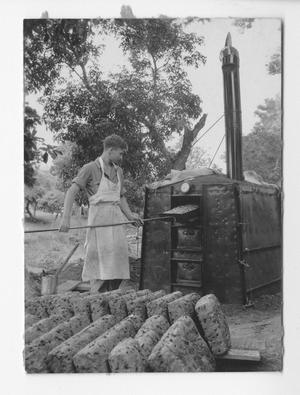 Primary view of object titled '[Man putting food in an outdoor oven]'.