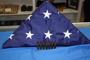 [Image of a triangular folded U.S. Flag and seven shell casings]
