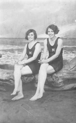 [Two young women with bob haircuts sitting on a driftwood log]