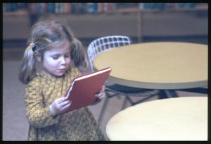 [Young Girl Examines a Book Cover]