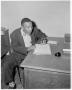 Photograph: [Man sitting at desk while writing on paper]
