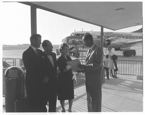Primary view of object titled '[Three men and a woman dressed in formal attire at an airport]'.