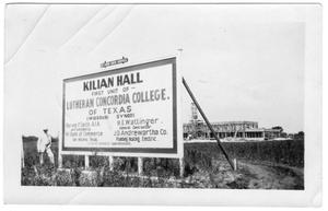 Primary view of object titled 'Man standing next to "Kilian Hall" sign'.