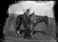 Photograph: [Man standing by a saddled horse]
