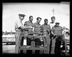 [Men viewing machine parts in front of Denton police car]