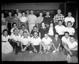 [League of bowlers pose in front of bowling lanes]