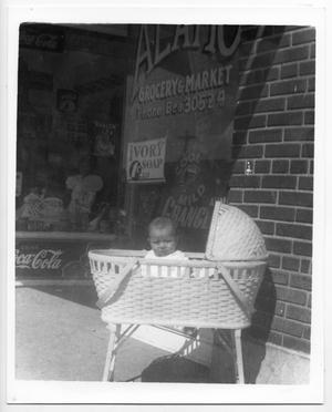 [Baby in bassinet in front of Alamo Grocery store]