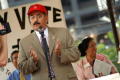 Primary view of [Hector Flores speaking while wearing suit and red hat]