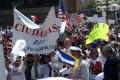 Primary view of [A man addresses the crowd while protesters raise flags and signs]