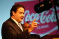 Photograph: [Man pointing with index finger in front of "Coca Cola" sign]