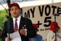 Thumbnail image of item number 1 in: '[Man in suit and red hat speaking at microphone in front of printed sign]'.