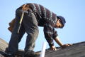 Photograph: [Man bent over and cutting surface of roof]