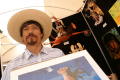 Photograph: [Man in straw hat holding artwork in front of black display board]