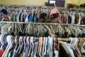 Primary view of [Three people stand among racks of clothing in Dallas charity]