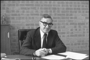 Primary view of object titled '[Unidentified man in glasses poses behind desk]'.